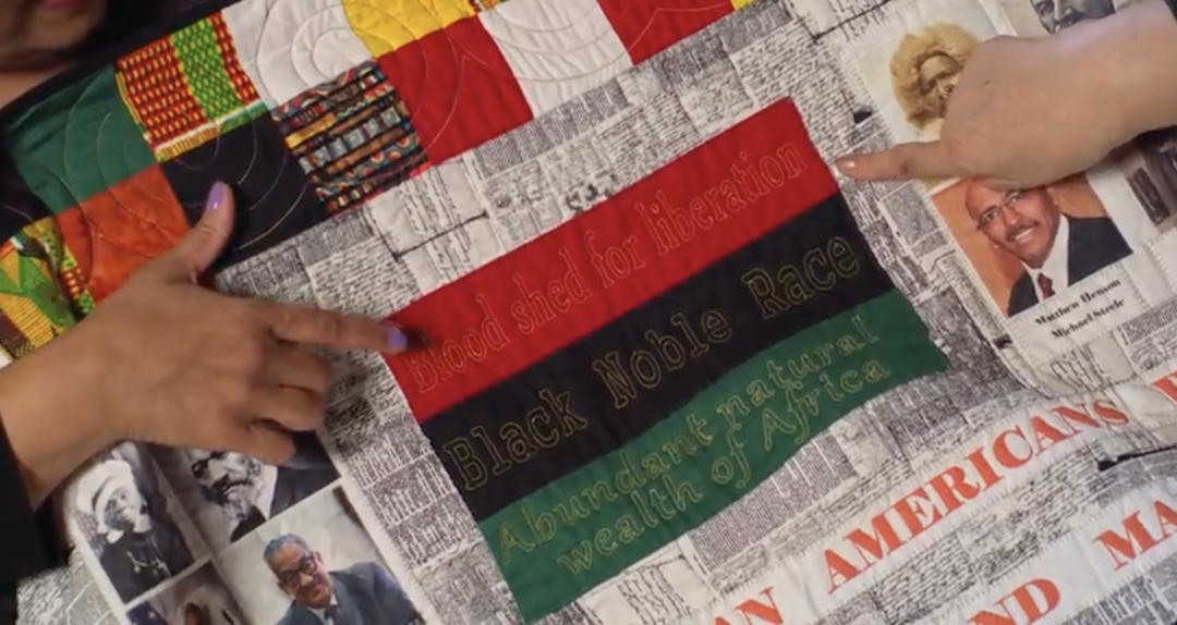 hands pointing to quilt with pan African flag