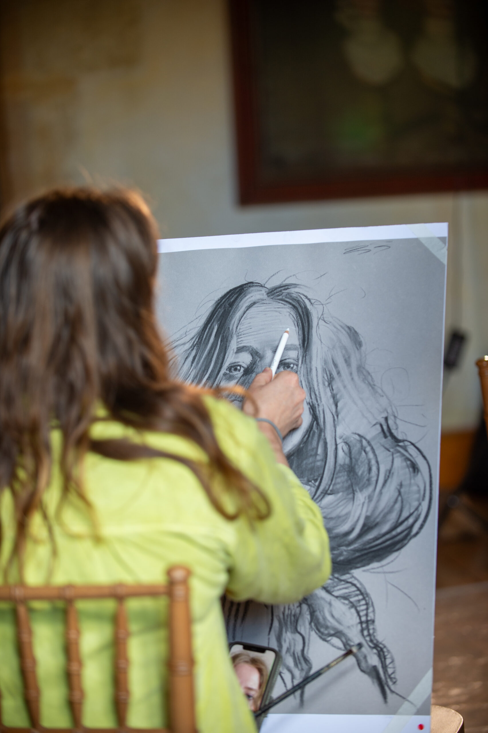 Person with long hair, back turned to viewer, sketching a person on paper.