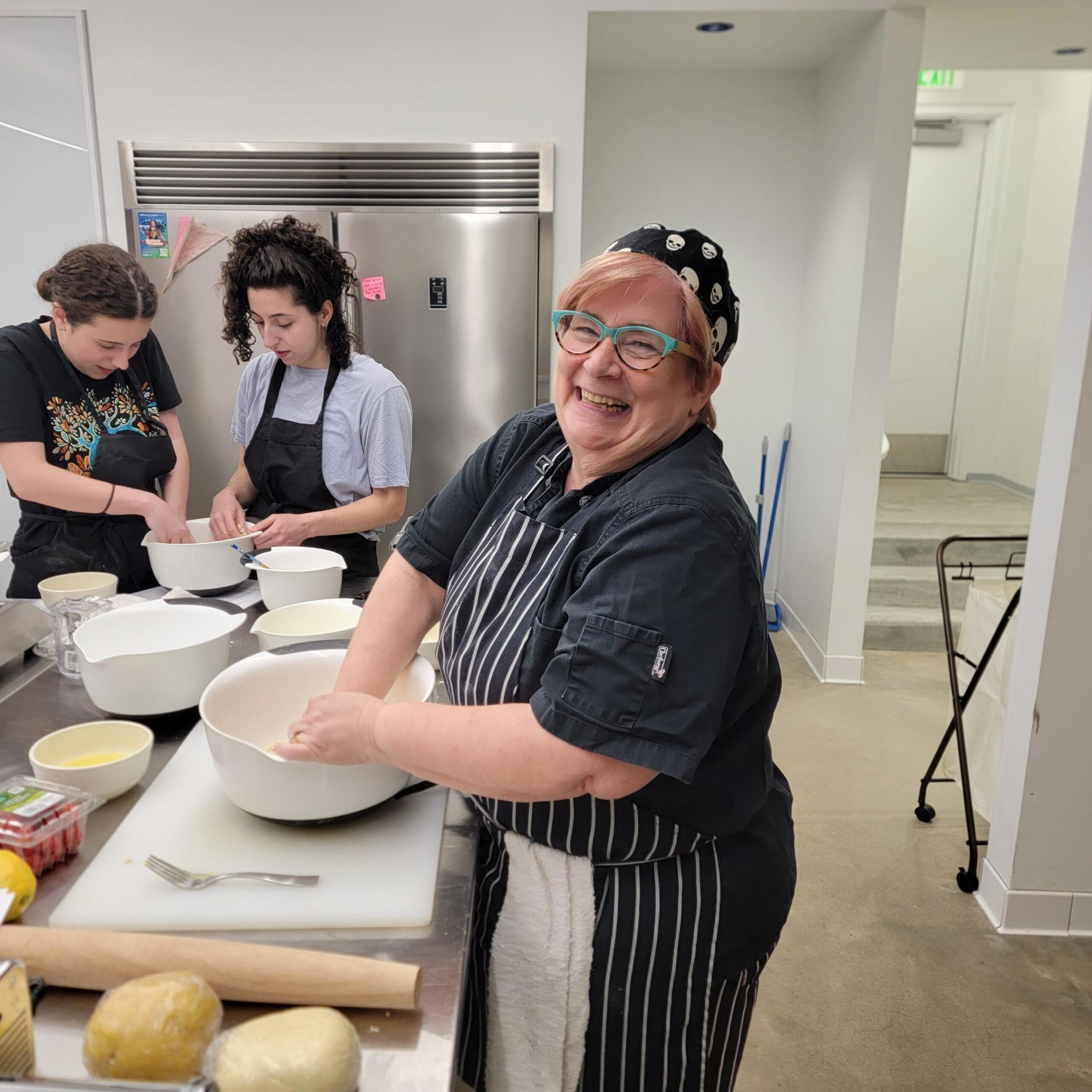 a human chef with pink hair is cooking in the teaching kitchen with students